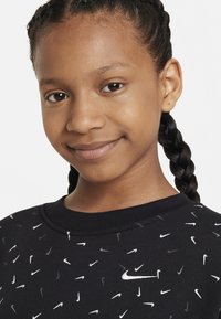 Felpa nera con loghi Nike bianchi e grigi sparsi, in materiale felpato, collo a giro e capelli intrecciati.