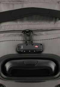 Maleta de viaje gris con exterior de textura suave, que presenta un cierre negro, mecanismo de bloqueo y un asa curva negra.