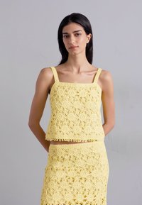 Ensemble deux pièces au crochet en jaune vif avec des motifs floraux, comportant un décolleté carré, des bretelles fines et un ourlet volé sur la jupe.