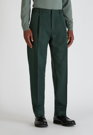 Grüne, plissierte Hose aus einem glatten Stoff, mit regulärer Passform und getragen mit schwarzen Schuhen. Maßgeschneiderter Schnitt mit Fronttaschen.