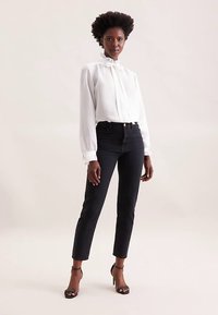 White long-sleeve blouse with a ruffled collar paired with high-waisted black jeans and black heeled sandals, featuring a slim-fit design.