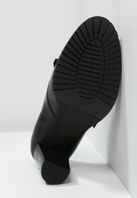 Tacón de cuero negro con una suela de goma texturizada. Presenta una forma cuadrada y un tacón de bloque resistente, mostrando un patrón de pisada detallado.