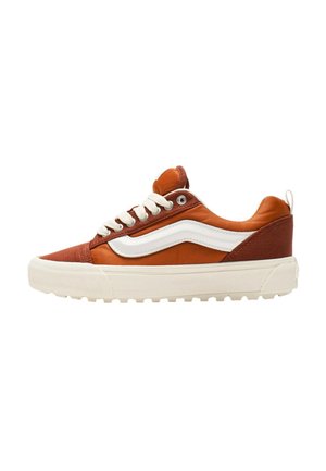 Zapatilla marrón y blanca con parte superior de lona y cuero, puntera redonda, cordones planos y suela de goma texturizada. Presenta una raya lateral distintiva.