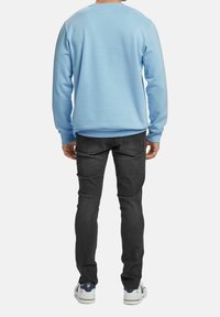 Felpa azzurra, colletto girocollo, polsini a coste, abbinata a jeans grigio scuro e sneaker bianche con accenti blu navy. Look casual e comodo.