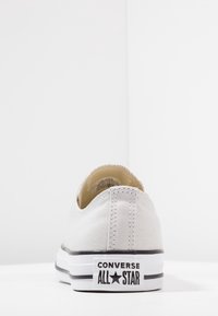 Baskets Converse en toile grise avec une semelle en caoutchouc blanche, présentant des accents noirs et le logo "Converse All Star" sur le talon.