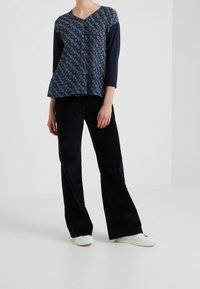 Tummansinisen kuviollinen paita, jossa on kolme neljännestä hihoista, yhdistetty mustiin samettisiin leveisiin housuihin. Materiaali on pehmeä ja teksturoitu, minkä ansiosta se täydentää asua.