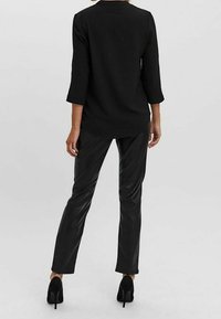 Maglietta nera a maniche lunghe con orlo arrotondato, abbinata a pantaloni in pelle nera aderenti e scarpe con tacco alto. Texture liscia e design semplice.