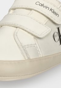 Λευκό sneaker Calvin Klein με ιμάντες βέλκρο και λογότυπο τυπωμένο στο πλάι κοντά στη σόλα και τον ιμάντα.