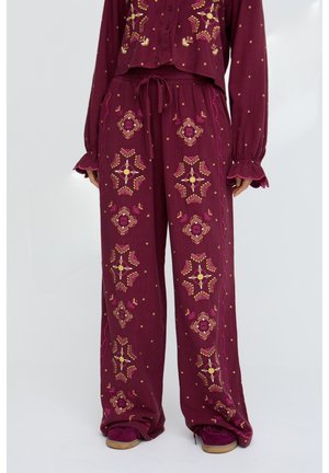 Weinrote Hosen mit weitem Bein und gelb-pinken geometrischen Stickereien, elastischem Bund mit Kordelzug, getragen mit passendem langärmeligen Oberteil und weinroten Schuhen.