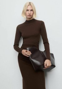 Top marrone a collo alto in maglia abbinato a una gonna marrone aderente, che tiene una borsa strutturata in pelle marrone scuro. Design minimalista con texture liscia.