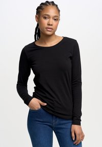 Mustat pitkähihainen t-paita, joka on valmistettu sileästä kankaasta, pyöreä pääntie, slim fit -malli, ja yhdistetty sinisiin farkkuihin, korostaen modernia rentoa tyyliä.