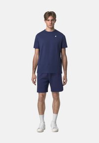 T-shirt blu navy e pantaloni corti coordinati in cotone. La t-shirt ha un collo rotondo e un piccolo logo sul petto. Sneakers bianche e calzini corti.