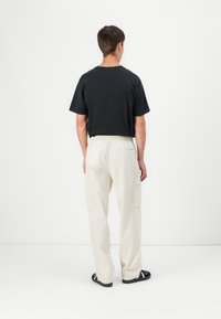 Svart kortärmad T-shirt kombinerad med lösa, off-white cargobyxor som har två sidofickor, mot en neutral bakgrund.