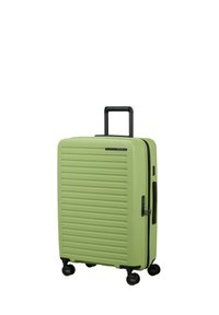 Grüne Hartschalenreisetasche mit horizontalen Rillen, schwarzem Reißverschluss, seitlichem Griff und vier Rädern für einfache Mobilität.