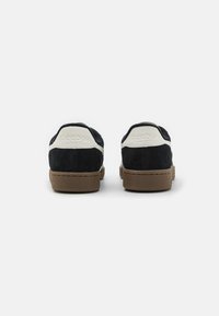 Zapatillas de ante negro con acentos blancos, suela de goma marrón texturizada y logotipo de Reebok estampado en el talón. Diseño de perfil bajo.