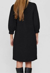 Svart texturerad klänning med medellång design, som har trekvartslånga puffärmar och rund halsringning. Slät, mjuk tyg.