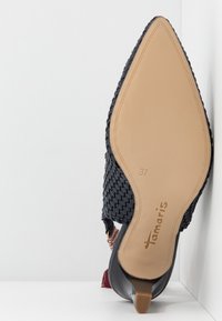 Chaussure à bout pointu de couleur noire avec une tige tissée et une semelle lisse beige. Présente un accent décoratif rouge et le nom de la marque en relief. Taille 37 visible.