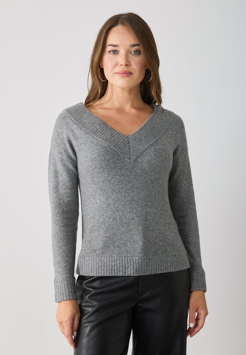 Maglione grigio in lana con scollatura a V ribattuta e polsini a coste, caratterizzato da una vestibilità rilassata e una consistenza morbida. Abbinato a pantaloni neri.