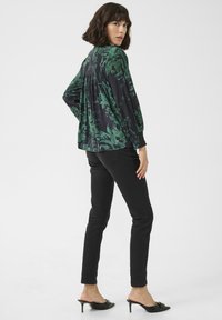Flowy blouse with dark green floral pattern on a black background. Paired with fitted black jeans and black heeled mules.
