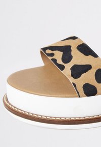 Ruskeat perusliuku-sandaalit, joissa on leopardikuvioinen päällinen. Ominaisuuksina leveä hihna, sileä pohja ja valkoinen pohja, jossa on teksturoitu ruskea reuna.