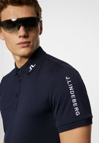 Marinblå polo med knappslå, korta ärmar och kontrasterande axellogo. Texturerad krage och broderad logotyp på ärmen.