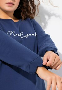 Felpa color navy con la scritta bianca in corsivo "New Casual" sul petto, con polsini a volant testurizzati e colletto classico.