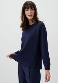 Granatowy pulower z długim rękawem, charakteryzujący się luźnym krojem, okrągłym dekoltem i bocznymi rozporkami u dołu; wykonany z miękkiego materiału.