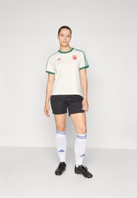 White soccer jersey with green accents and logo, black shorts, white socks with blue stripes, and black cleats. Simple design, athletic fit.