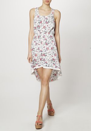 Robe sans manches à imprimé floral avec une taille élastique, un ourlet asymétrique et un tissu léger en blanc, ornée de fleurs roses et bleues.