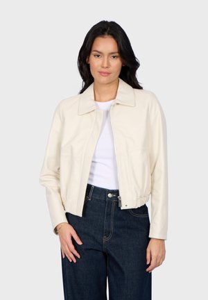 Cream faux leather jacket with a collared neckline, cropped fit, and zipper closure. Paired with dark denim pants. Smooth texture.