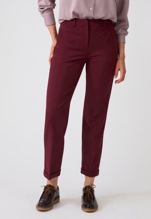 Persona che indossa pantaloni color burgundy a gamba stretta risvoltati alle caviglie, scarpe stringate marrone scuro e una camicia a righe a maniche lunghe infilata dentro.