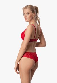 Czerwony koronkowy komplet bielizny składający się z biustonosza typu balconette z regulowanymi ramiączkami oraz pasujących przezroczystych majtek typu hipster z kwiatowymi wzorami.