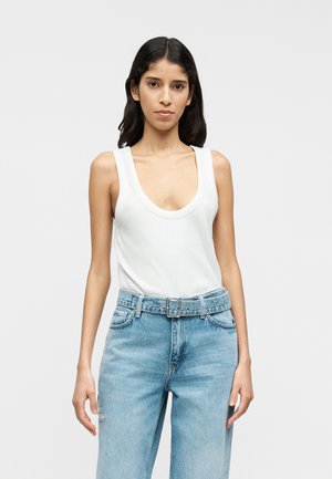 Camiseta sin mangas blanca con escote pronunciado, combinada con jeans de tiro alto en azul claro con cinturón. Tela suave y ajuste relajado.