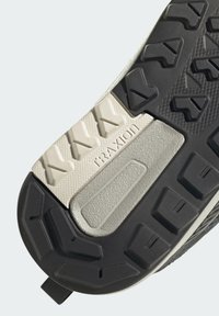 Černá a šedá gumová podrážka tenisek s texturovanou gumou, trojúhelníkovým vzorem a embosovaným logem "TRAXION" na hladké, světlé části.