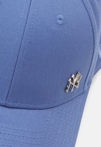 Cappello blu realizzato in tessuto testurizzato, con una forma strutturata e un logo argentato sul lato. Dettagli di cucitura visibili in tutto il cappello.