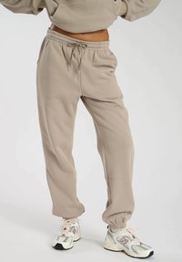 Beige sweatpants lavet af blødt stof, med en elastisk talje og snoretræk, sidelommer og snævre cuffs ved anklerne.