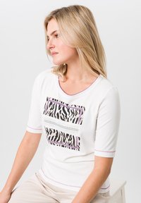 Witte korte mouwen top met een zwart-wit zebraprint ontwerp, voorzien van paarse accenten en decoratieve stiksels langs de halslijn en mouwen.