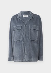 Chaqueta de camisa de pana azul con dos bolsillos frontales, cierre de botones y cuello tradicional. Presenta una textura suave y tela acanalada.