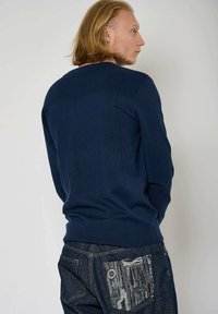 Pull en tricot bleu marine avec détail côtelé aux épaules, coupe ajustée et col rond. Porté avec un jean sombre avec une poche arrière texturée.