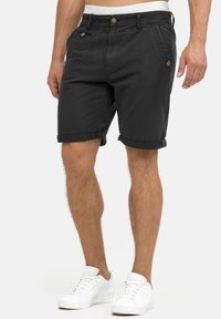 Shorts en coton noir avec ourlets retournés, dotés d'une fermeture à bouton et de poches latérales. Associés à des baskets blanches. Design et coupe simples.
