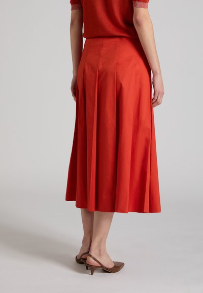 Mujer vistiendo una falda roja acampanada hasta la rodilla combinada con zapatos destalonados marrones de tacón bajo, vista desde atrás.