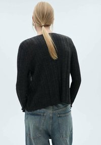 Pull noir en maille côtelée avec un design court, une finition texturée et un col rond, assorti à un jean en denim bleu clair.