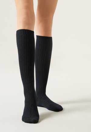 Knähöga ribbade strumpor i mörk marinblå, tillverkade av mjukt material. Har strukturerade vertikala linjer och en tätt sittande, elastisk mudd upptill.