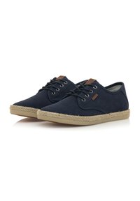 Zapatos de cordones azul marino hechos de tela texturizada con una suela de yute natural. Presentan detalles en cuero marrón cerca de los cordones.