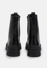 Botas de piel negra hasta el tobillo con cremalleras en la parte trasera, suelas de goma gruesa y costuras detalladas en los laterales. Acentos negros texturizados.