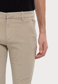 Beżowe spodnie sztruksowe o dopasowanym kroju, z płaskim pasem, bocznymi kieszeniami i gładką fakturą. Szlufki na paski w talii.