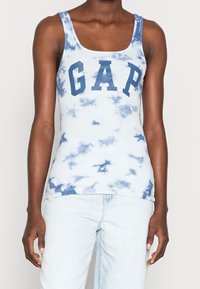 Débardeur bleu clair avec motif tie-dye blanc et logo "GAP" bleu vif sur la poitrine. Confectionné en tissu côtelé, les bretelles sont larges.