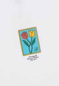 Deux fleurs, une rose rouge et une tulipe jaune, avec des feuilles vertes à l'intérieur d'un rectangle bleu avec une bordure jaune et un texte en cursive en dessous sur un tissu blanc.