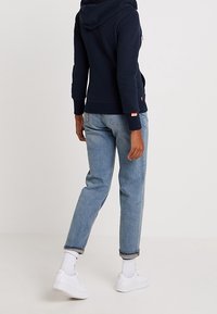 Felpa con cappuccio blu navy, design casual con polsini a costine, abbinata a jeans dritti azzurri e sneakers bianche. Tessuto liscio.