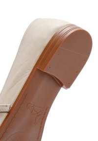 Beige synthetic shoe with a rounded toe, a textured upper, and a brown rubber sole featuring a subtle logo and horizontal grooves.